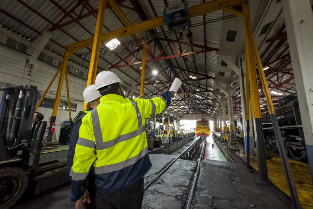 Male worker in uniform and helmet operates a crane on factory. Industrial production, metalwork engineering, power machines manufacturing